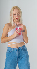 Young attractive blonde woman in a white top and blue jeans with a cocktail in her hands on a white background