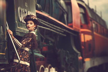 Beautiful girl in a historical retro dress on a background of an old steam locomotive, steampunk,...
