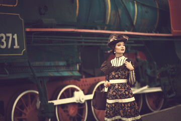 Obraz na płótnie Canvas Beautiful girl in a historical retro dress on a background of an old steam locomotive, steampunk, at the railway station.