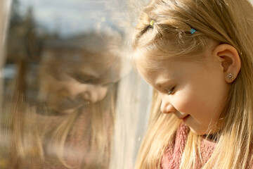 A small child near the window at home. The child is safe, sunlight on the face