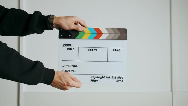 A punch on a cinematic slate or clapper board. Close-up of a hand holding an empty slate board and slapping it against a white background. White studio background. Opening and closing slate board for