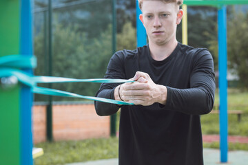 Fitness trainer exercises the upper half of the body in the morning on an outdoor workout court with the help of expanders and rubber bands. Chest and shoulder muscles warm-up
