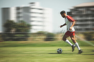 Football, fitness and soccer player running on the field to score goals in a sports match or training game outdoors. Blur, Brazil and young athlete doing cardio exercise, practice or workout on grass