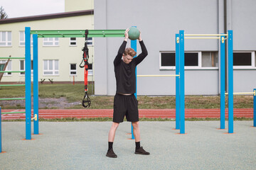 Professional athlete stands in a squatting stance holding a medicine ball to streamline core training and I throw them against the ground. Outdoor workout court