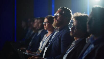 Young Bearded Man Attending a Political Conference, Sitting in Crowded Hall. Journalist Taking Notes and Writing an Article on Laptop Computer. Writer Listening to a Motivational Speaker.
