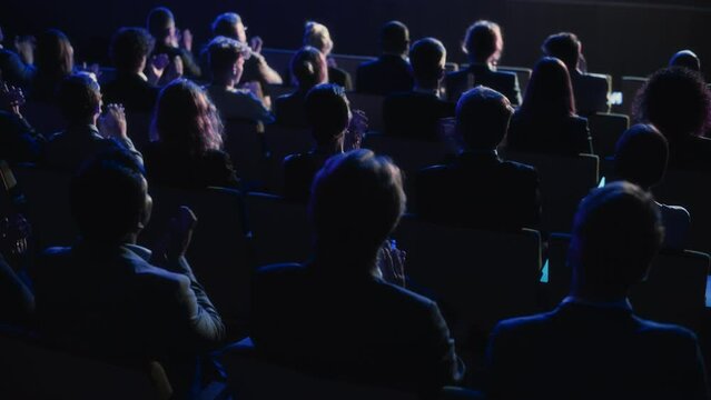 Crowd of Smart Tech People Applauding in Dark Conference Hall During a Motivational Keynote Presentation. Business Technology Summit Auditorium Room Full of Delegates. Footage from Behind.