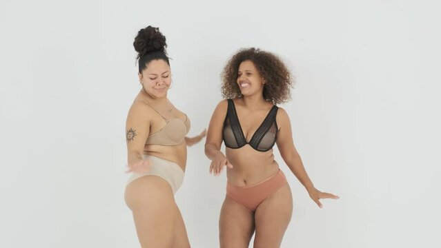 Smiling diverse female plus size models in lingerie dancing in studio