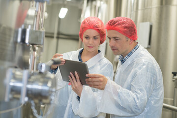 brewery workers wearing hairnets looking at tablet screen