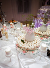 Obraz na płótnie Canvas An appetizing candy bar for holiday guests stands on a table with a white tablecloth, with sweets, candles and various utensils, in the banquet room.