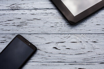 Elements of devices, a tablet and a mobile phone lie on a light wooden textured surface.