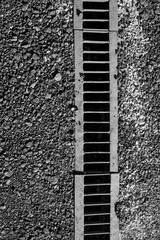 Iron sewer mesh for sewage on an asphalted road with rubble, Black and white textured photo.