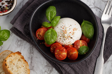 Fresh Italian burrata with tomatoes and basil on plate on marble table, close up. Burrata cheese ball made from mozzarella and cream. Healthy food
