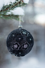 Hanging black glitter Christmas ball on spruce and over blurred background