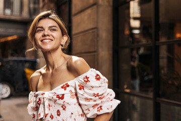 Smiling caucasian young lady with smile on her face spends weekend outdoors in summer. Blonde looks away, wears blouse. Mood concept, leisure