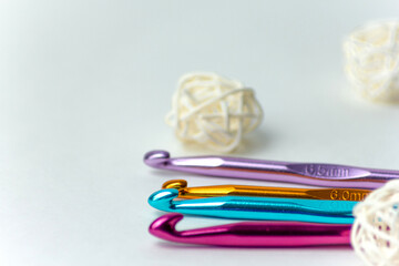 Multicolored crochet hooks of different diameters on a white background with white rattan balls. On...