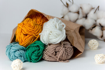 Multicolored threads in a kraft bag on a white background with a cotton ball and white rattan...