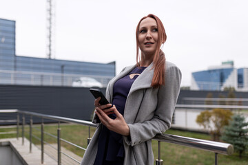 portrait of a business red-haired woman businessman with a mobile phone in his hands on the background of an office building