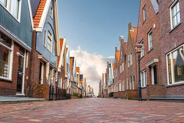 Gordijnen Smalle Straten low angle view of cobbled street and typical buildings in dutch town of Volendam against blue sky  © Christian Horz