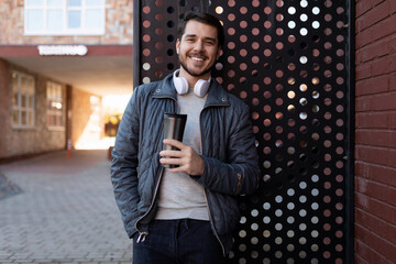 stylish man 35 years old in headphones with a glass of coffee looking at the camera on the street