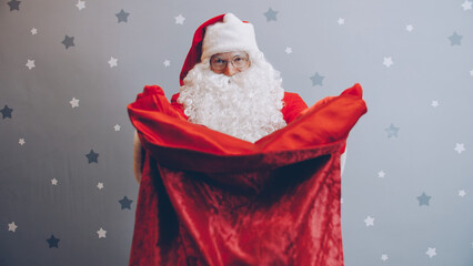 Portrait of Santa stretching arms with bag of gifts to camera on New Years day offering presents on holiday. Events,celebrations and Christmas concept.