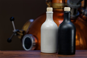 Gin distillery, white and black ceramic gin bottles on a wooden counter in front of the copper...