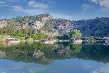 Fototapeta premium The rock-cut temple tombs of the ancient city of Kaunos in Dalyan, Muğla, Turkey. Beautiful view of Dalyan river with reed beds, excursion boats and carved tombs in the background.