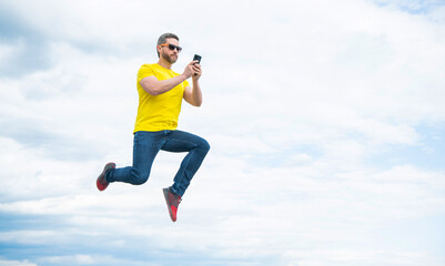 Fototapeta premium man jump and chatting on smartphone on sky background. copy space
