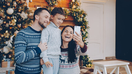Joyful parents and child are talking making online video call on New Year day using smartphone, people are wearing warm Christmas style clothing.