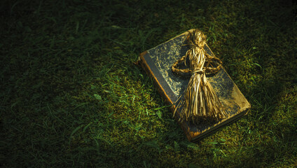 An old book on witchcraft and a voodoo doll lie on the green grass. Items for witchcraft and secret spells. An antique doll made of straw.