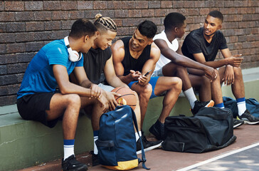 Basketball, sports and phone with a team talking on a court bench after a game or match outdoor. Teamwork, technology and conversation with a man athlete group chatting after exercise or fitness