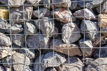 rocks in metal cage netting. river defence barrier. grey rock material textured background.