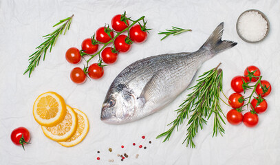 Fresh uncooked dorado fish or sea bream with lemon herbs cherry tomatoes and spices on white backing paper on white background.