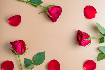 Border frame made of red roses and flower petals on beige background. Flat lay, top view. Frame of flowers.