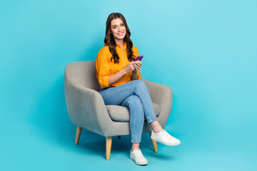 Fototapeta na wymiar Full body photo of cheerful pretty lady sit chair hold use telephone isolated on blue color background
