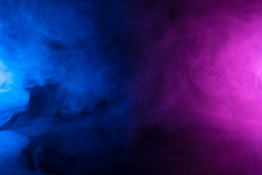 Clouds of colorful smoke in blue and purple neon light swirling on black table background