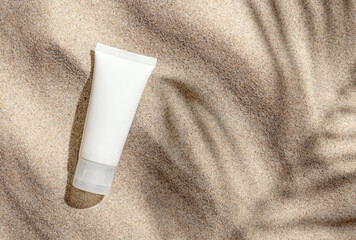 White ceam tube on beige sand top view, palm leaf hard shadow. Cosmetic mockup
