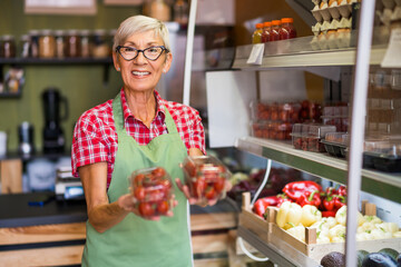 Mature woman works in fruits and vegetables shop. She is examining goods.