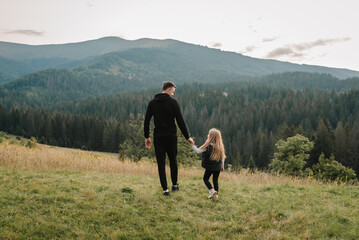 Dad and daughter walk in the mountains enjoy the sunset and look at nature. Back view. The young...
