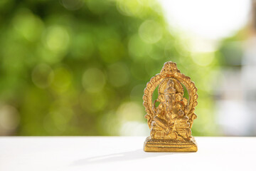 An old golden Ganesha statue on a white wooden table with nature background with blank for copy...