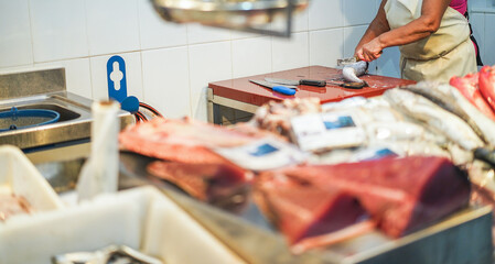 Fish monger preparing fish inside seafood market - Soft focus on woman knife cutting fish