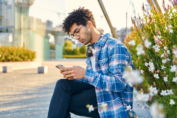 Curly haired middle eastern man wearing eyeglasses using mobile phone, communication online. Social media concept 