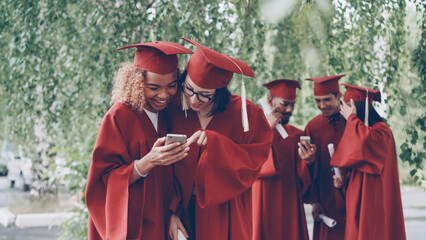 Beautiful young women graduating students watching smartphone. Modern technology, millennials and...
