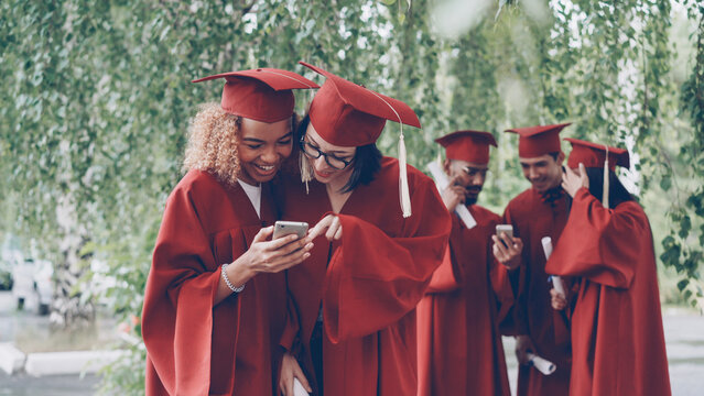 Beautiful young women graduating students watching smartphone. Modern technology, millennials and education concept.