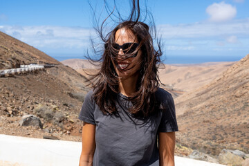 Portrait of young smiling woman face partially covered with flying hair in windy day standing at mountain