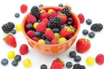 Ceramic brown bowl of mixed forest fruits (blueberries, raspberries, blackberries and strawberries), cherries and grapes.  White background full of mixed fruits