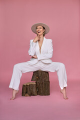 Beautiful happy woman looking away while posing on tree stump against purple background