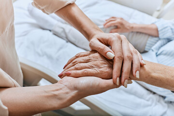 Relative holding trembling hand of senior woman with Parkinson's disease lying in hospital bed at...