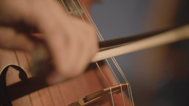 Super close footage of a man playing a cello with a bow with a shallow depth of field.