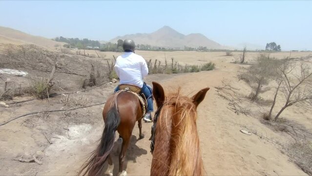 Rider POV, Two equestrian horse riders galloping through arid farmland