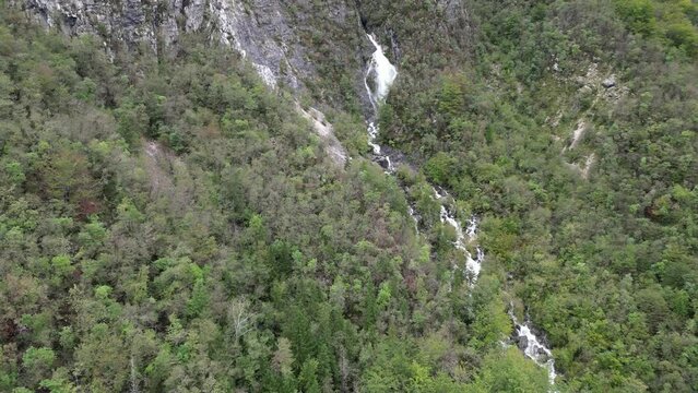 Waterfall cascading through trees Lake Bohinj Slovenia pull back reveal drone aerial view